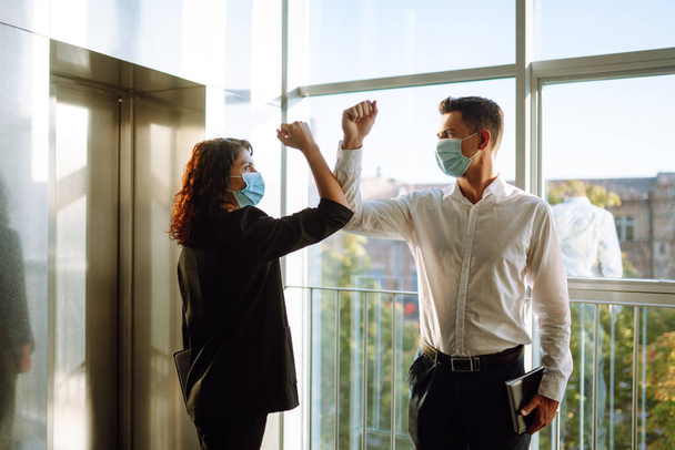Elbow greeting to avoid the spread of coronavirus (COVID-19). Two colleagues wearing face masks bumping elbows while greeting each other at work in office.  - Valokuva, kuva