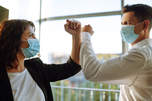 Elbow greeting to avoid the spread of coronavirus (COVID-19). Two colleagues wearing face masks bumping elbows while greeting each other at work in office.  - Foto, immagini