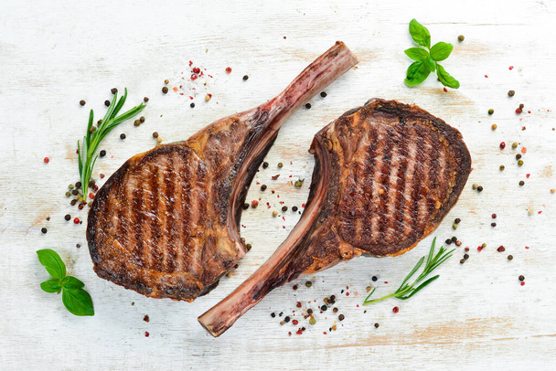 Tamahavk steak on the bone with spices and herbs. On a white wooden background. Top view. Free copy space. - Valokuva, kuva