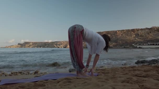 Mujer de 40 años practicando yoga en la playa de arena en la madrugada - Metraje, vídeo