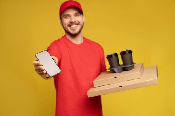 Young man holding pizza and smartphone isolated on yellow. - Foto, Imagen