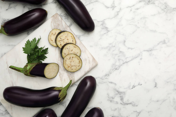 Cut and whole raw ripe eggplants on white marble table, flat lay. Space for text - Φωτογραφία, εικόνα