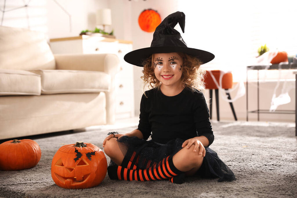 Cute little girl with pumpkin wearing Halloween costume at home - 写真・画像