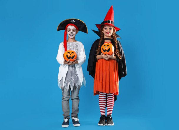 Cute little kids with pumpkin candy buckets wearing Halloween costumes on blue background - Fotó, kép