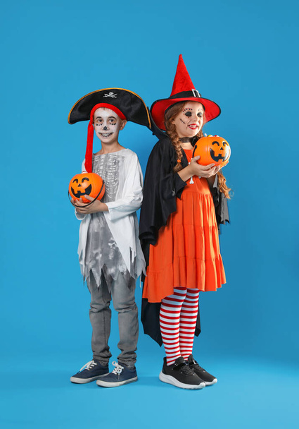 Cute little kids with pumpkin candy buckets wearing Halloween costumes on blue background - Photo, image