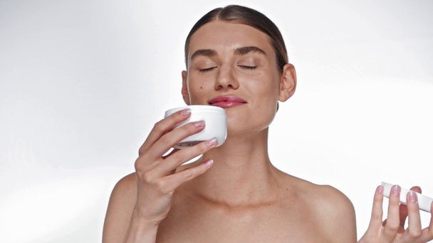Jeune femme adulte ouverture récipient et odeur de crème cosmétique sur blanc - Séquence, vidéo