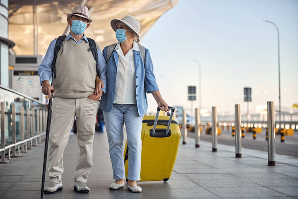 Пожилая супружеская пара в масках в аэропорту - Фото, изображение