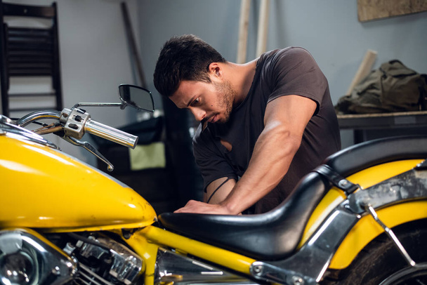 A young mechanic tuning a motorcycle in an auto repair shop. Hobbies and work activity. - Foto, Imagem