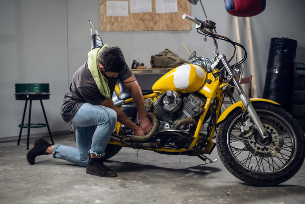 Silný motorkář si opravuje motorku v garáži. Interiér dílny. - Fotografie, Obrázek