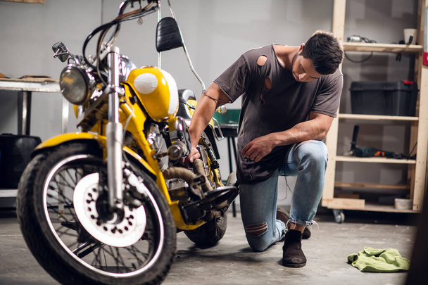 Сучасний молодий чоловік у футболці і джинсах займається діагностикою велосипедів у ремонтному магазині або гаражі
. - Фото, зображення