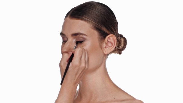 Donna che applica eyeliner con spazzola cosmetica su occhio di modello isolato su bianco - Filmati, video