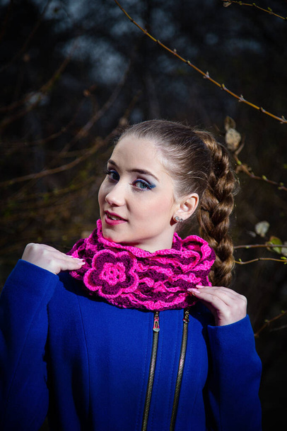 Fiatal lány kék kabátban és rózsaszín csíkos kötött sznob sállal és virágos melltűvel. Női őszi és téli ruházat és kiegészítők koncepció. - Fotó, kép