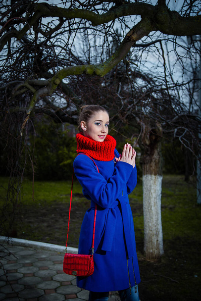 Mavi ceketli kırmızı çantalı, pamuklu atkı takan genç bir kız. Kadın sonbahar ve kış kıyafetleri ve aksesuar konsepti. - Fotoğraf, Görsel