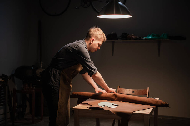 een jonge getalenteerde schoenmaker in de werkplaats is bezig met de handmatige productie van schoenen van leer. - Foto, afbeelding