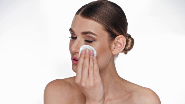 Young adult woman with cotton pad removing makeup isolated on white - Footage, Video