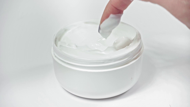Visão de perto da mulher aplicando creme cosmético do recipiente no branco - Filmagem, Vídeo