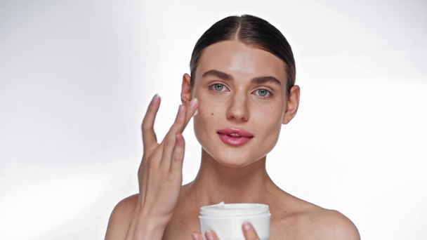 Souriant jeune femme adulte appliquant de la crème cosmétique sur la joue sur blanc - Séquence, vidéo