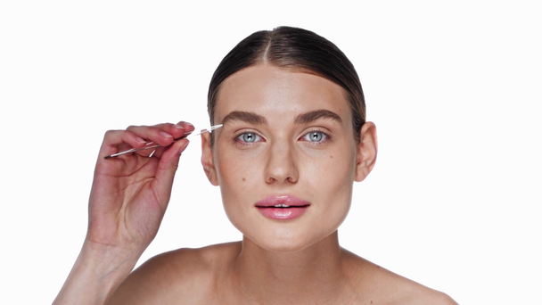 Jeune femme adulte arrachant les sourcils avec des pinces isolées sur blanc - Séquence, vidéo