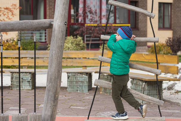 Un niño ágil sube una escalera de cuerda en una ciudad colgante en un patio de recreo - Foto, Imagen