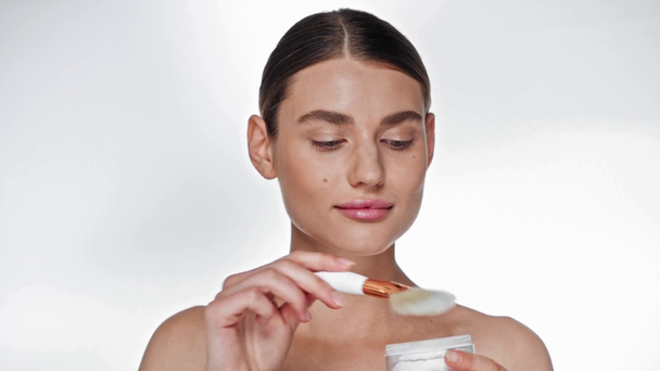 Mujer adulta joven positiva aplicando polvo facial en las mejillas sobre blanco - Metraje, vídeo