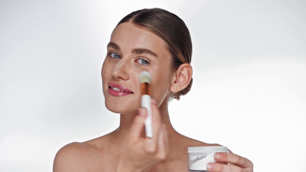 Young adult woman with cosmetic brush applying highlighter on face on white - Metraje, vídeo