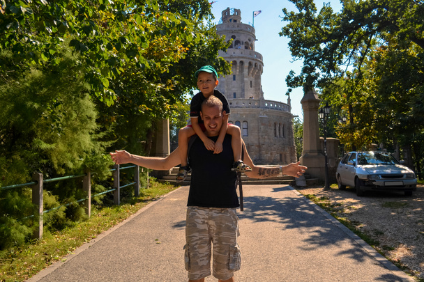 Mutlu, gülümseyen bir oğul, Janos Hill 'deki tarihi kulenin yanında gülen bir babanın omuzlarında oturuyor. Budapeşte, Macaristan - Fotoğraf, Görsel