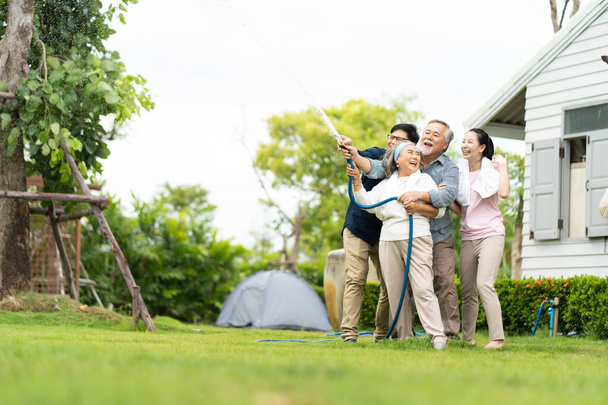 Asian family happy smiling and watering green cultivated plants with a garden hose at home. Happy family concept. 4 people father Mather sun daughter. - 写真・画像