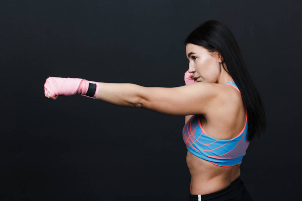 Sportsman muay thai strong woman boxer posing in training studio at black background. - Photo, Image
