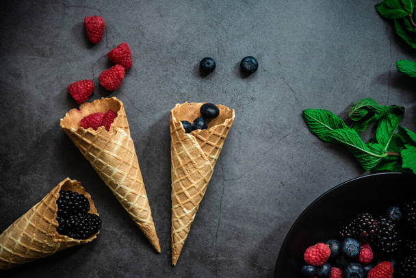 Top view of fresh berries and in waffle cones on dark stone background. Concept healthy food and desert. - Photo, Image