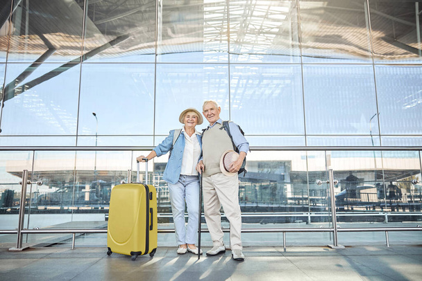 Pleased aged couple standing near the airport building - Foto, imagen