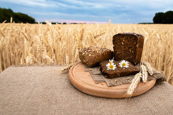 Organikus élelmiszer - kenyér fekszik az asztalon, a háttérben a búzamező. Mezőgazdasági élelmiszer-háttérrel. - Fotó, kép