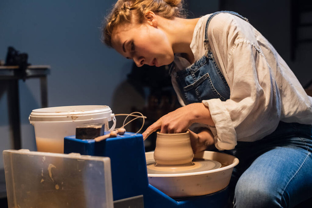 een ervaren pottenbakker een meisje in een kunst Studio maakt een pot van klei met haar handen. - Foto, afbeelding