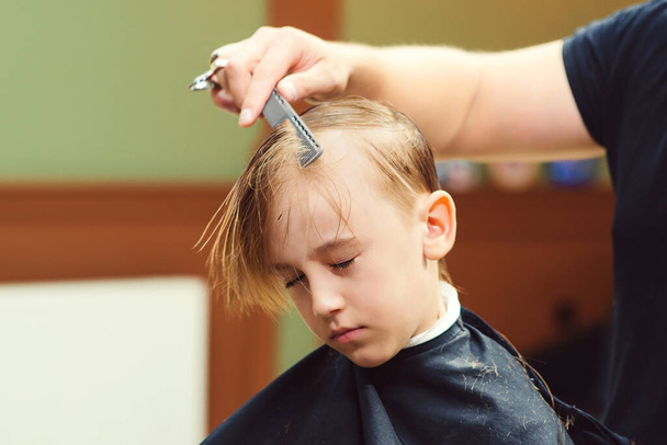 かわいい男の子が理容室で美容師に散髪している。理髪師は子供の髪型をしている。はさみ付きの美容師。理髪店だ。子供の頃。若い男の子のための新しい髪型. - 写真・画像