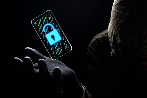 Kilit açma simgesini, bilgisayar korsanının elinde siyah bir eldiven, hackleme ve internet siber suç kavramının üzerinde yüzen akıllı telefon ekranında yeşil ikili kodla kapat - Fotoğraf, Görsel