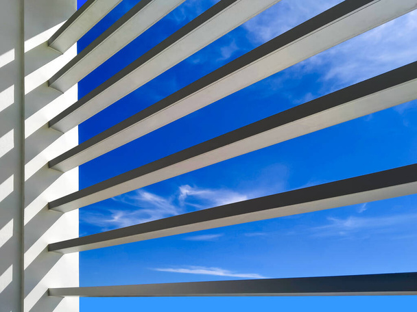 Światło słoneczne na listwie przeciwsłonecznej powierzchnia biurowca na tle błękitnego nieba, niski kąt widzenia od wewnątrz budynku - Zdjęcie, obraz
