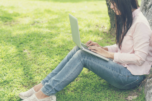 Ázsiai nő ül zöld park laptoppal. Nő dolgozik laptop boldog vállalkozó üzleti használ notebook kézzel gépelés billentyűzeten otthoni iroda alatt coronavirus karantén időszak - Fotó, kép