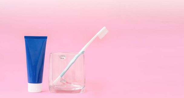 Blue toothpaste tube and toothbrush in transparent glass with gradient lighting on pastel pink background, close up with copy space - Photo, Image
