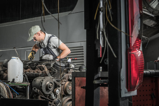 Кавказский автомобильный техник в свои 40 лет ремонтирует и восстанавливает старый тяжелый грузовой дизельный двигатель. Рабочий цеха автомобильной промышленности. - Фото, изображение