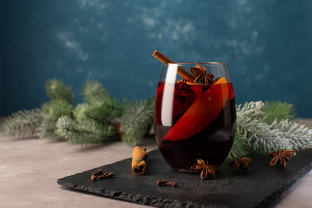 Christmas hot drink-Mulled wine with oranges,cinnamon,anise stars and cloves spice on festive Christmas background.Christmas festive card with tree branches on blue background with copy space. - Фото, зображення