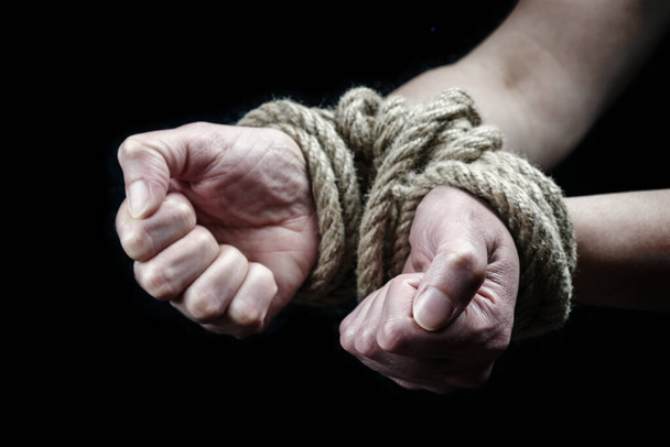 Les mains d'une victime attachées avec une corde rugueuse sur le fond noir. Cessez d'abuser du concept de violence - Photo, image