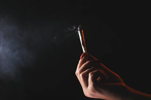 Donna mano tenuta sigaretta in un fumo su sfondo nero. Fumo cannabis. Uso medico. - Foto, immagini