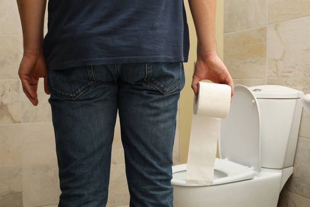 Мужчина стоит возле туалета и держит туалетную бумагу - Фото, изображение