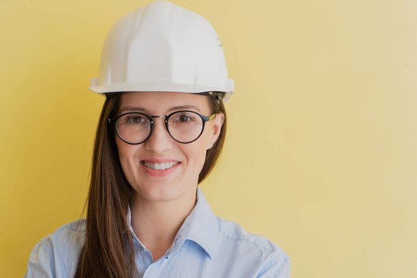 Portrait of smiling beautiful tatar woman engineer in construction helmet and glasses isolated on yellow background - Valokuva, kuva