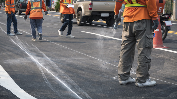 Nízký úsek skupiny silničních dělníků pracují na značení čáry pro malování provozu barevné čáry na asfaltové silnici, zatímco stále jezdí po městě, zaměření na člověka na popředí - Fotografie, Obrázek