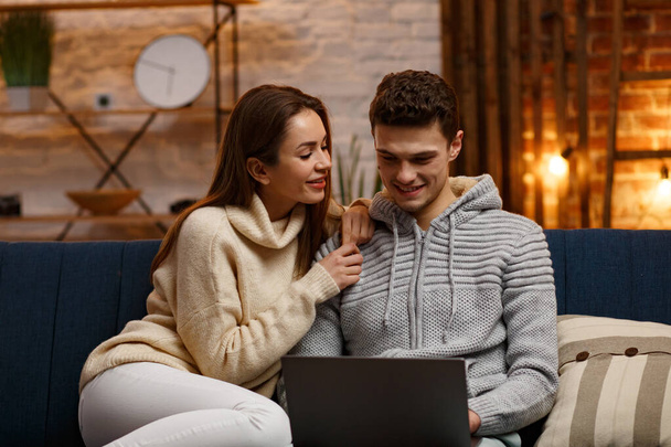 Winter holidays, Christmas celebrations, New Year concept. Portrait of beautiful smiling couple watching Christmas movie at home. Beautiful young couple at home enjoying spending time together - 写真・画像
