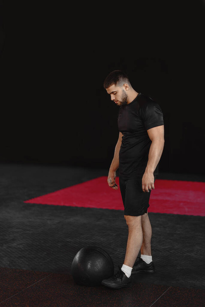 Jeune homme musclé en forme forte regardant le ballon de médecine et se préparer à l'entraînement Crossfit dans la salle de gym. - Photo, image