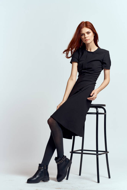 kobieta wysokie krzesło w pomieszczeniach pełna długość czarny sukienka czerwony włosy model buty - Zdjęcie, obraz