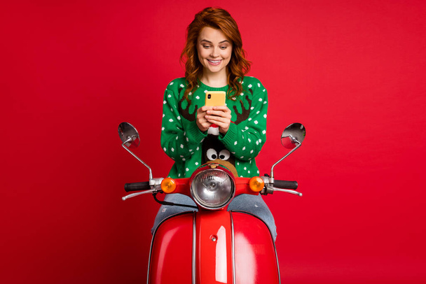 Photo portrait of scooter driver holding phone in two hands wearing ugly green jumper sweater isolated on bright red colored background - Φωτογραφία, εικόνα