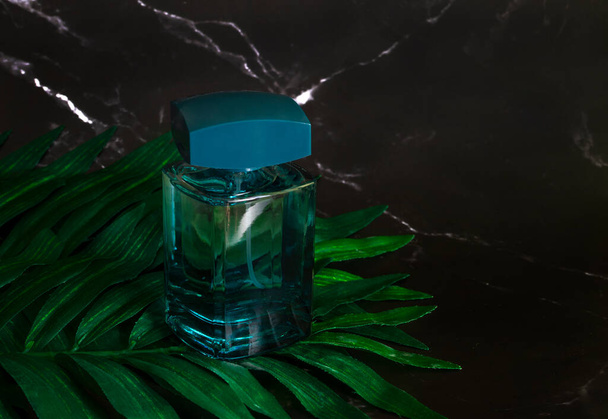 Bottle of men's perfume on a dark marble background with tropical leaves. - 写真・画像