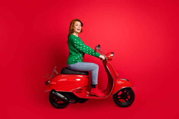Photo portrait side view of excited girl with open mouth riding scooter isolated on vivid red colored background - Foto, immagini